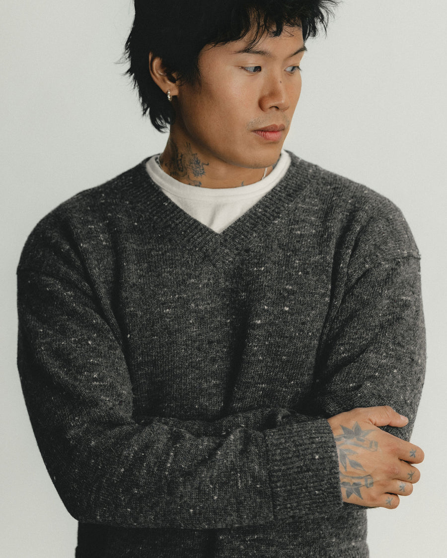 A man in a grey v-neck sweater crossed arms looks away.