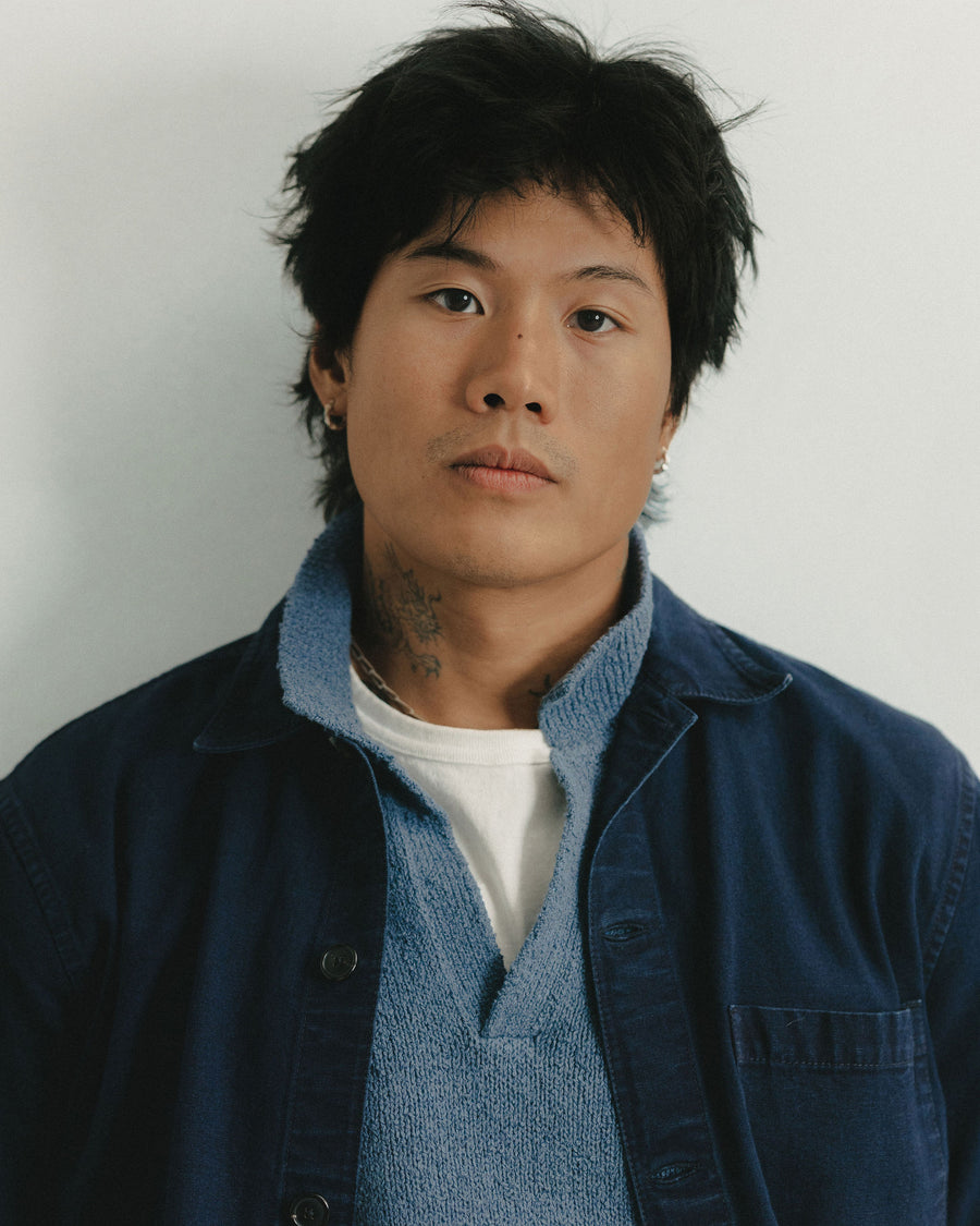 A close up portrait of a man in a dark blue jacket layered over a slate polo.