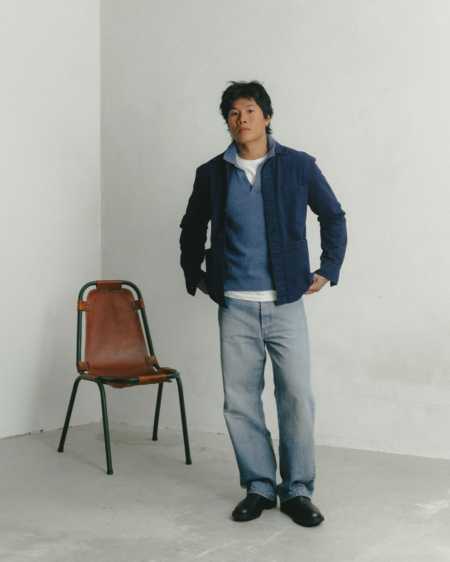 A man in a navy jacket layered over a slate blue knit polo looks into the camera.