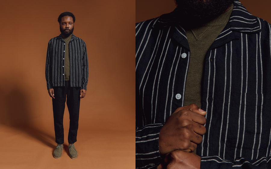 A man in a black striped shirt and olive sweater underneath.