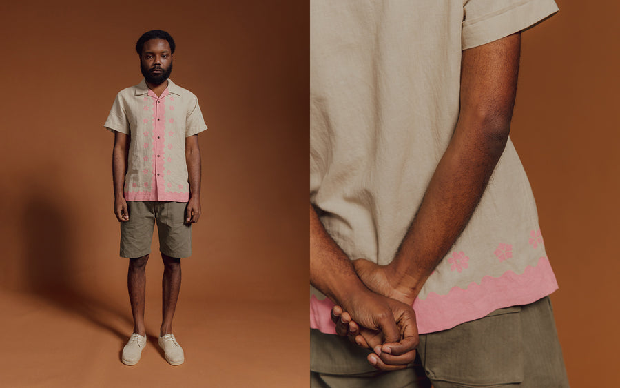 A man in a tan and pink short sleeve shirt and olive shorts.