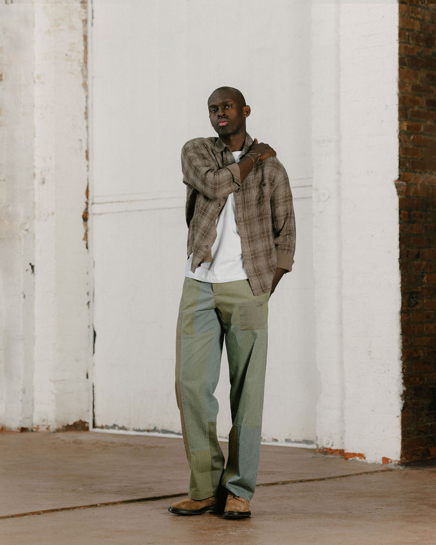 A man in a brown check shirt and olive patchwork pants.