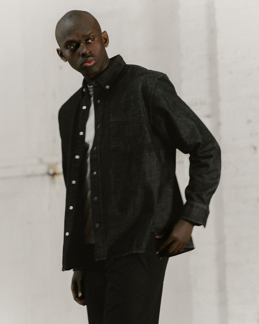 A closer photo of a man in a black denim button down.