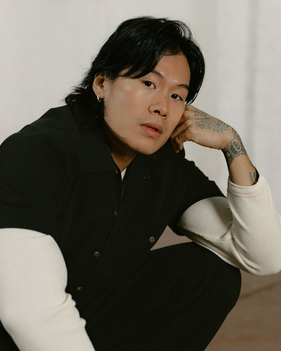 A portrait of a man in a black short sleeve shirt over a white thermal.