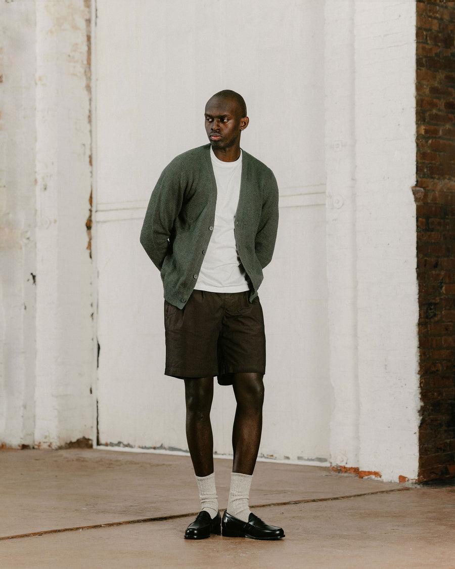 A man in an olive cardigan and brown shorts with loafers.
