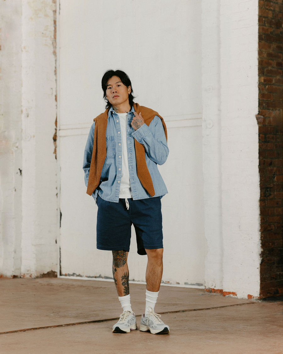 A man with a blue shirt and a tan sweater draped over his shoulders.