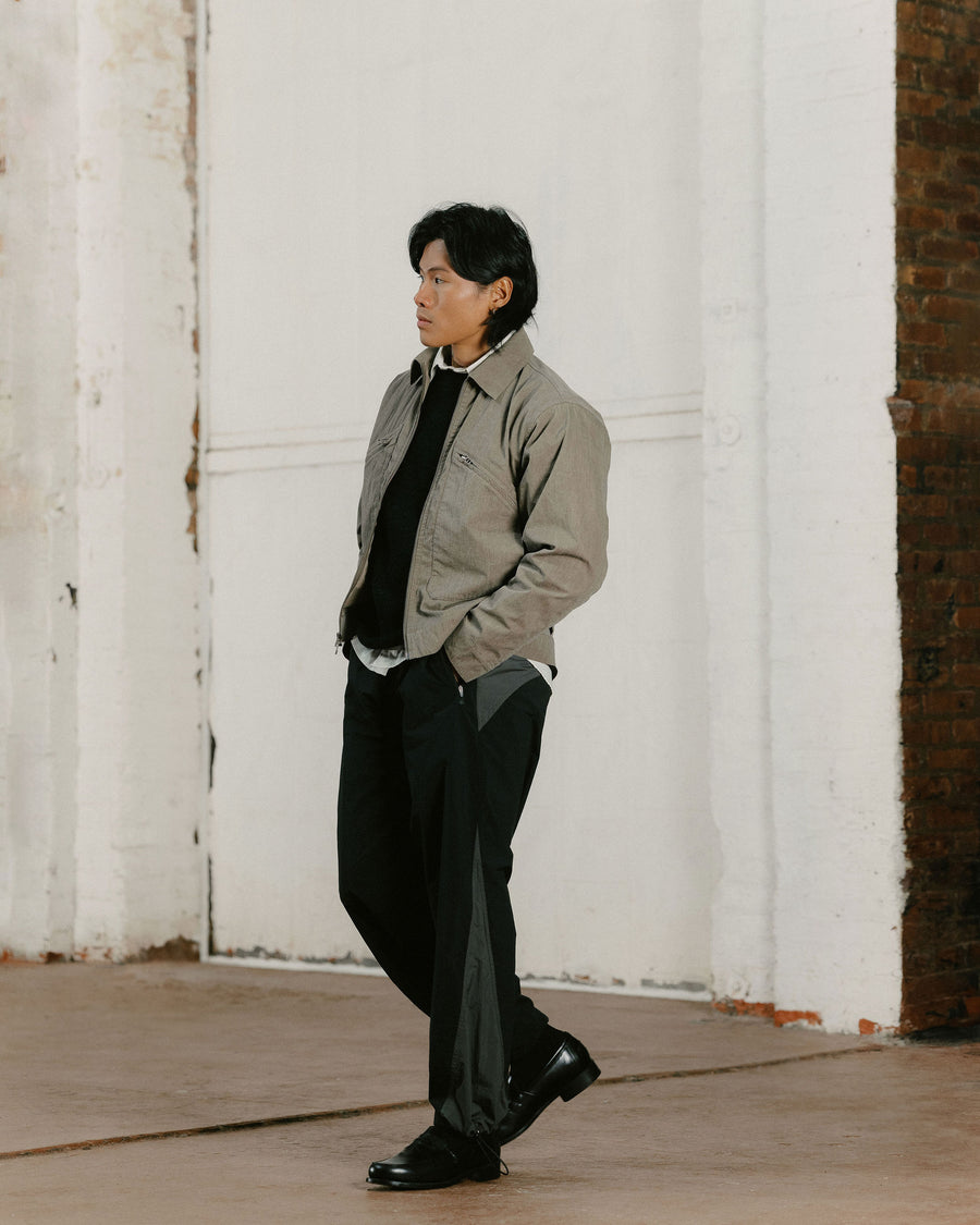 A man in a tan jacket and black track pants walks.