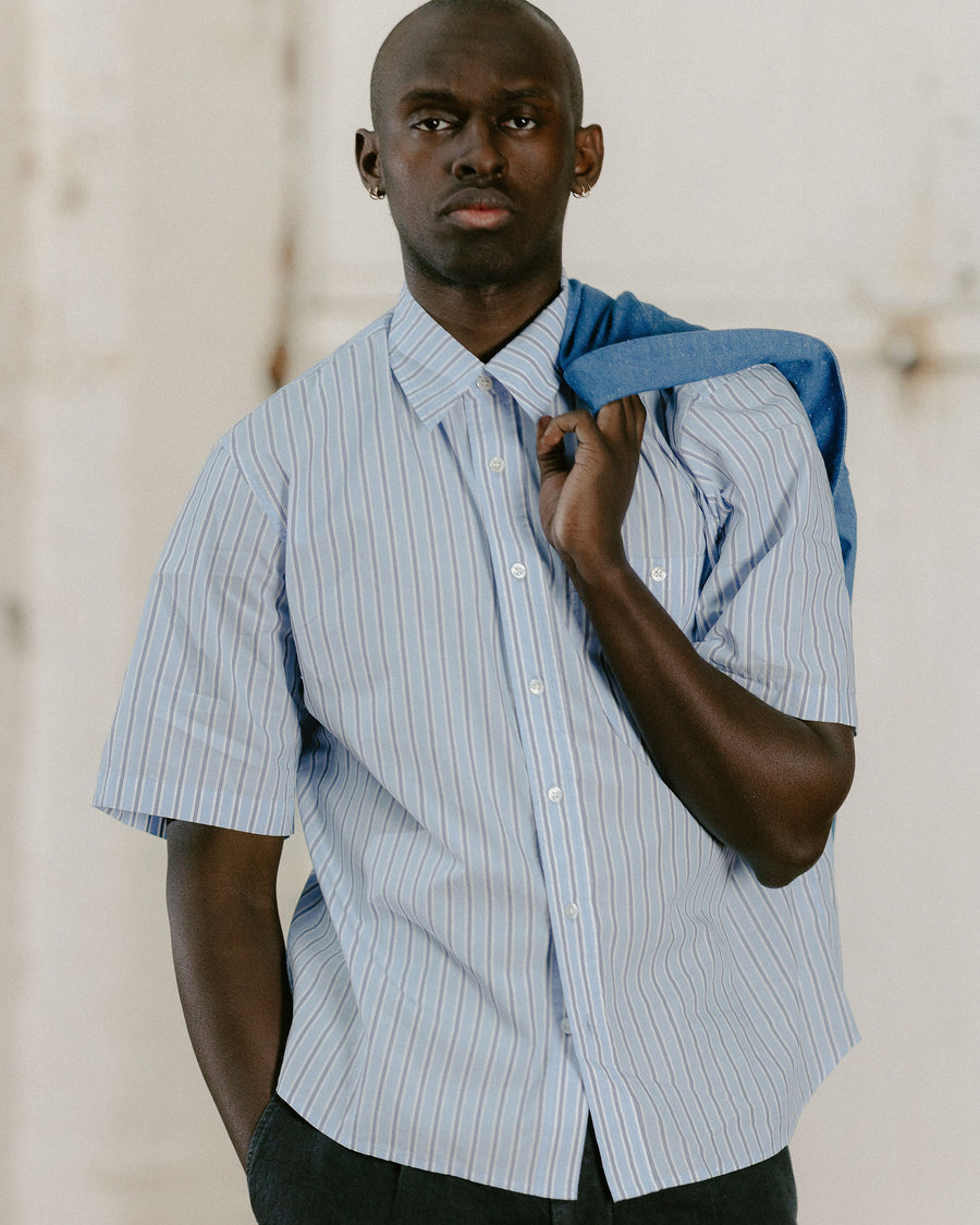 A man in a short sleeve blue striped shirt looks into the camera.