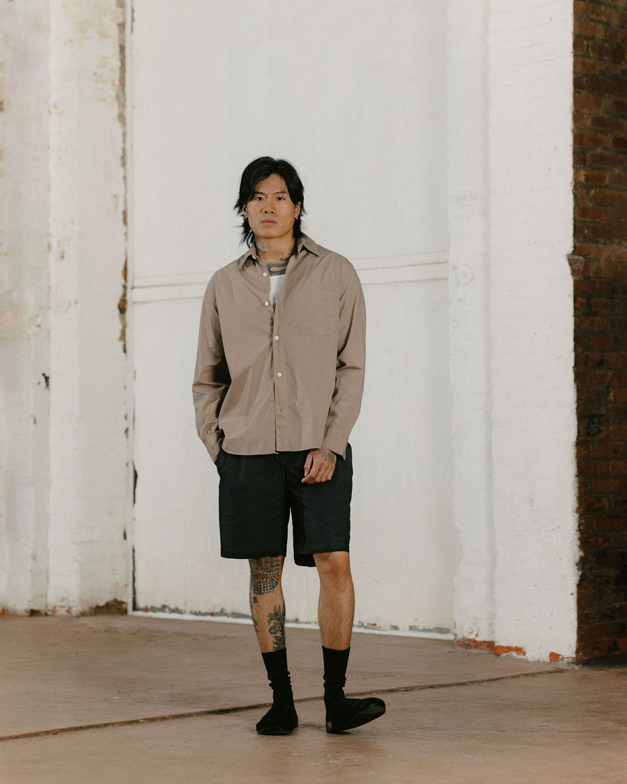 A man in a tan shirt and black shorts poses.