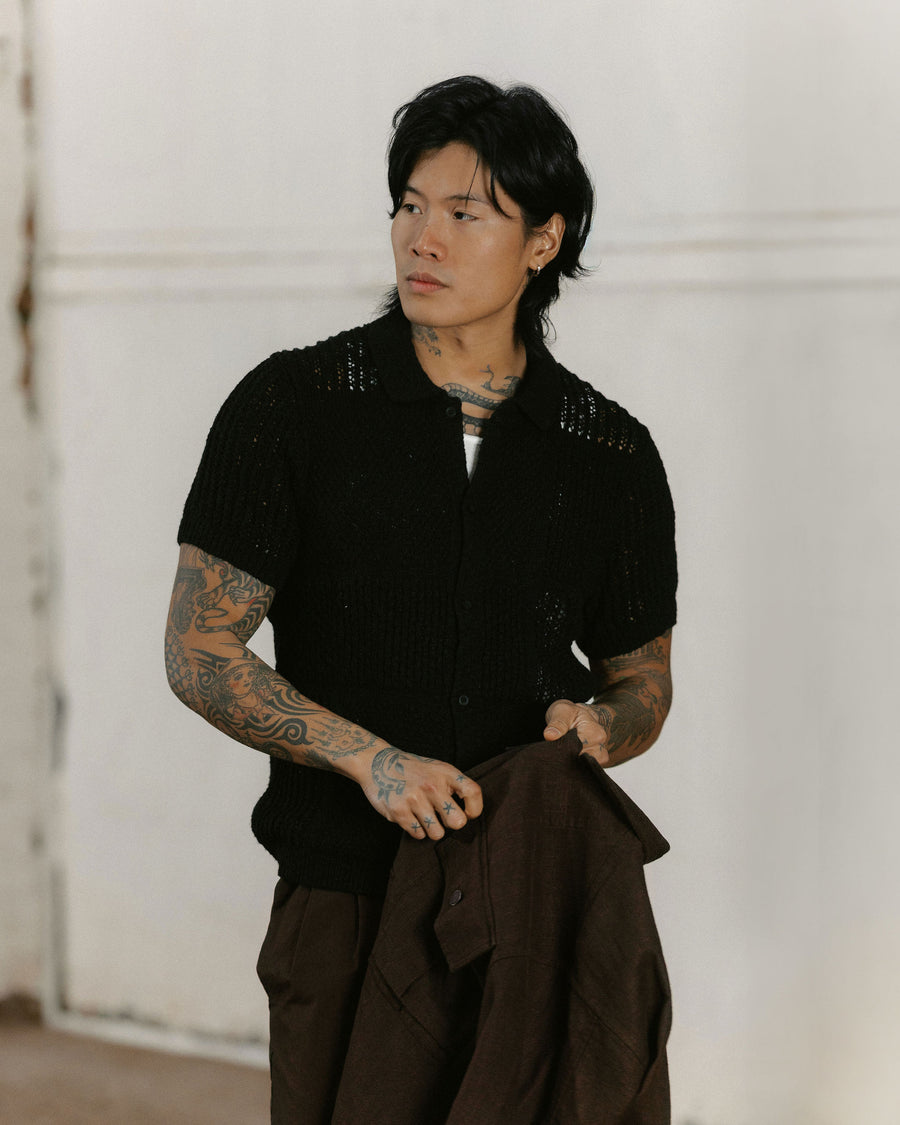 A man in a knit black shirt holds a brown jacket