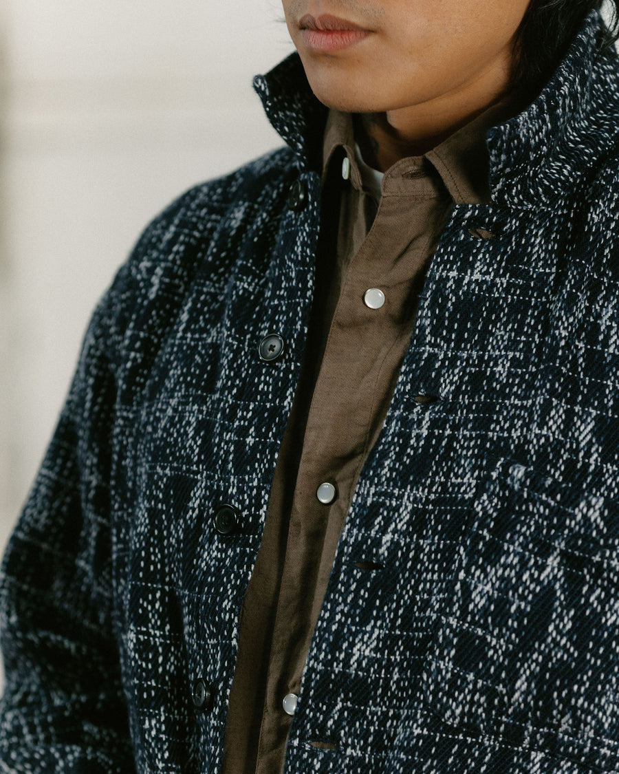 A close up shot of the texture on the black heathered jacket layered over a brown snap shirt.