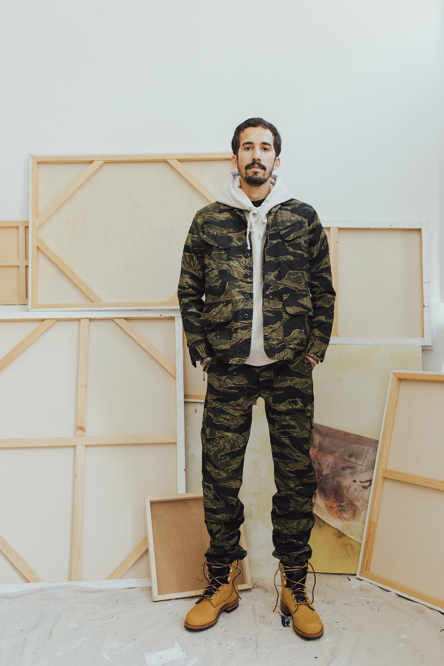 A man stands in front of a number of art canvases modeling clothing.