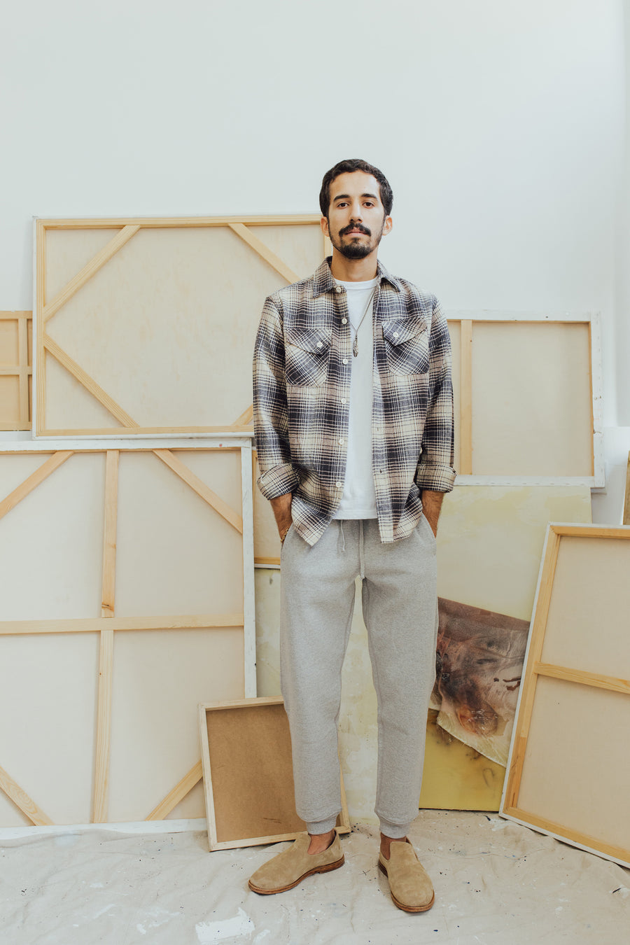 A man stands in front of a number of art canvases modeling clothing.
