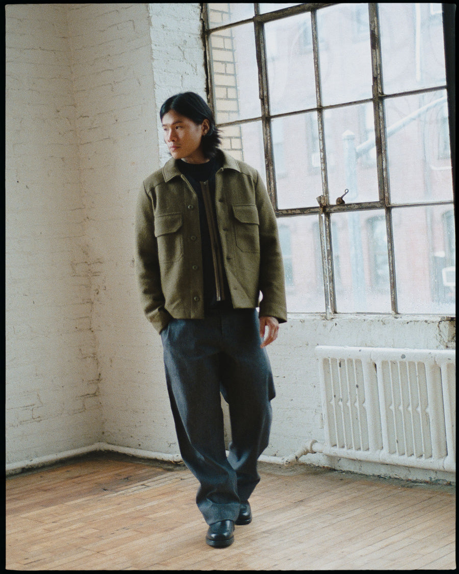 A man in a green wool shirt walks away from large windows.