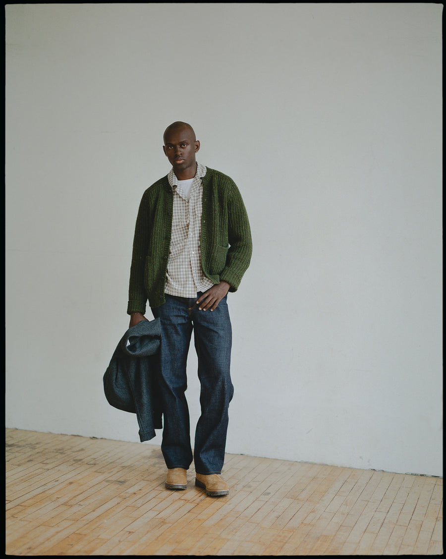 A man in a green button down cardigan and blue jeans.