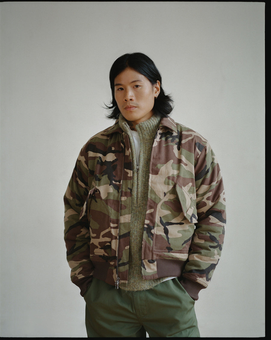 A man in a camo military jacket with a light green sweater underneath