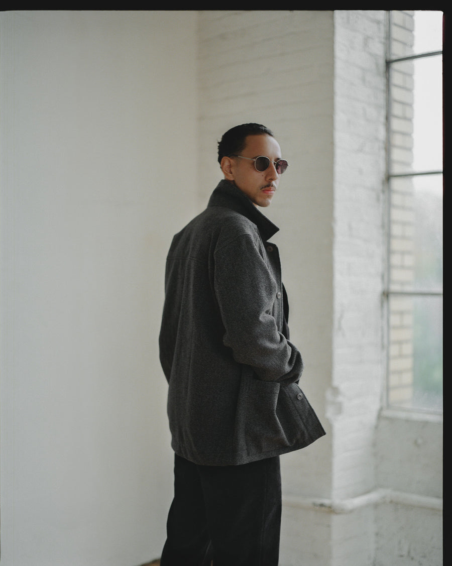 A man in sunglasses and a grey jacket looks back.