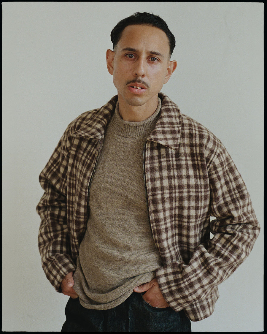 A man in a brown wool plaid jacket and light tan rollneck swaeter.