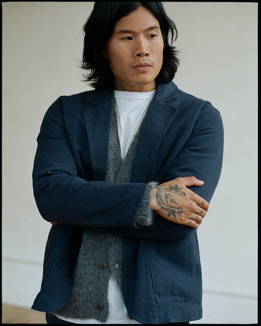 A man a navy blazer layered over a grey cardigan crosses his arms.