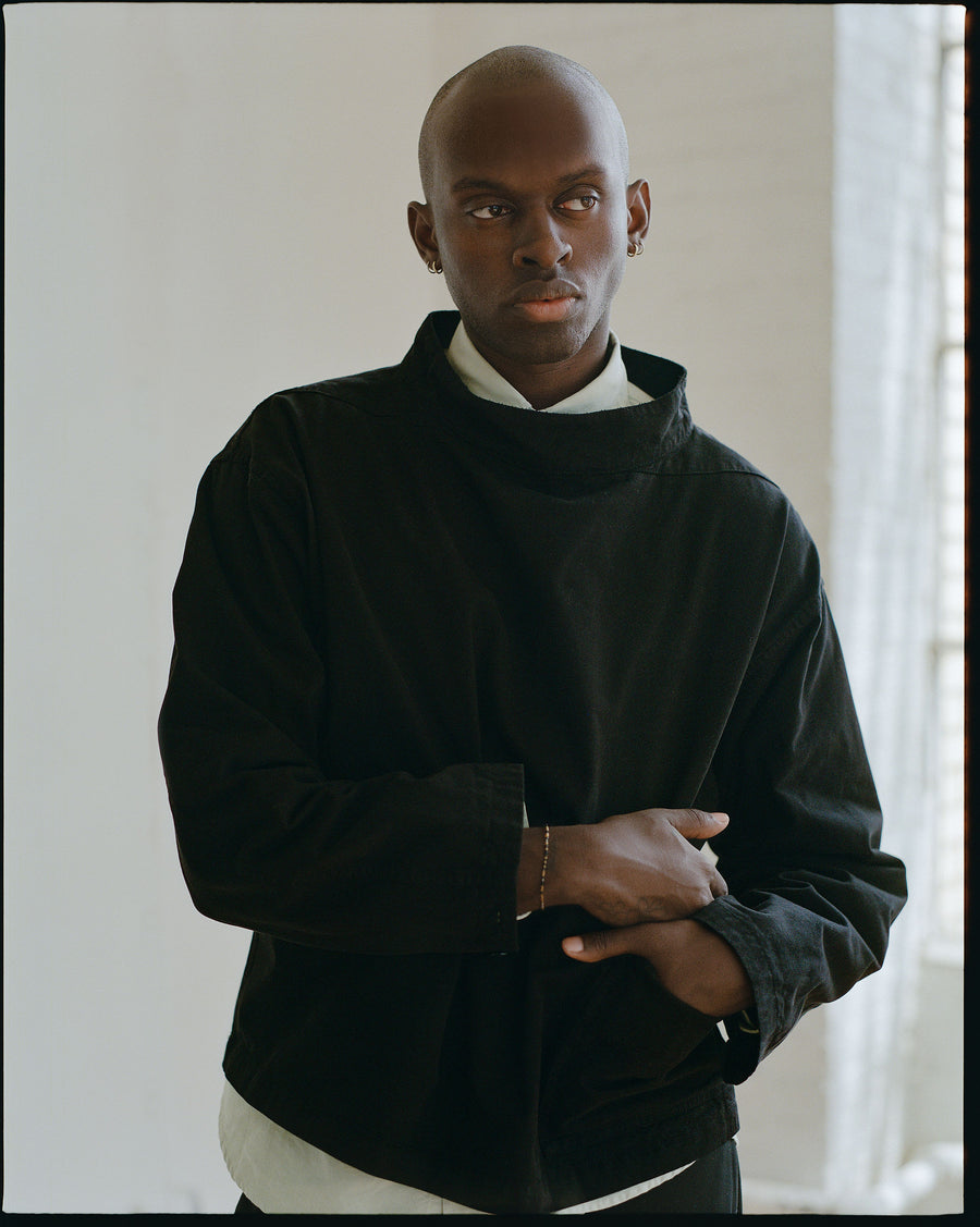 A man in a black smock layered over a button down shirt