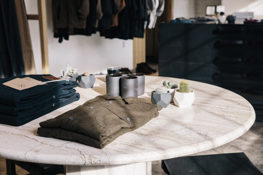 Folded shirts and jeans sit on a marble table, next to some mugs and succulents in pots.