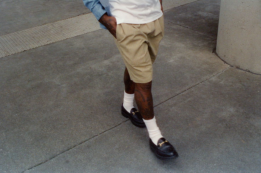 Someone in khaki shorts and black loafers walks across the street.