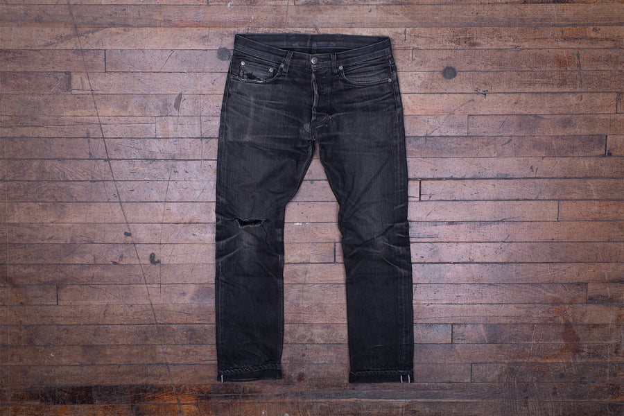 Front photo of a pair of worn-in black jeans laying on a wooden floor.