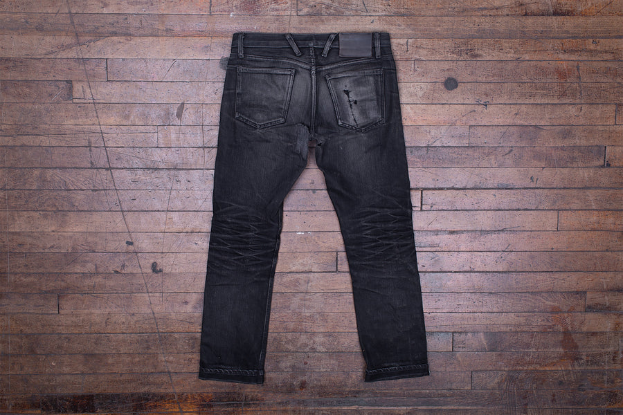 Back photo of a pair of worn-in black jeans laying on a wooden floor.