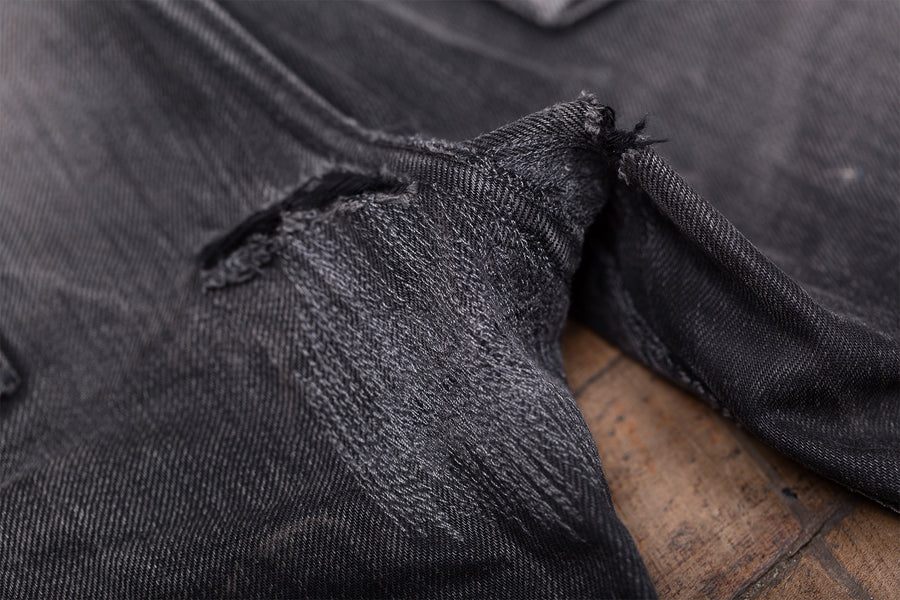 Detail photo of a pair of worn-in black jeans laying on a wooden floor.