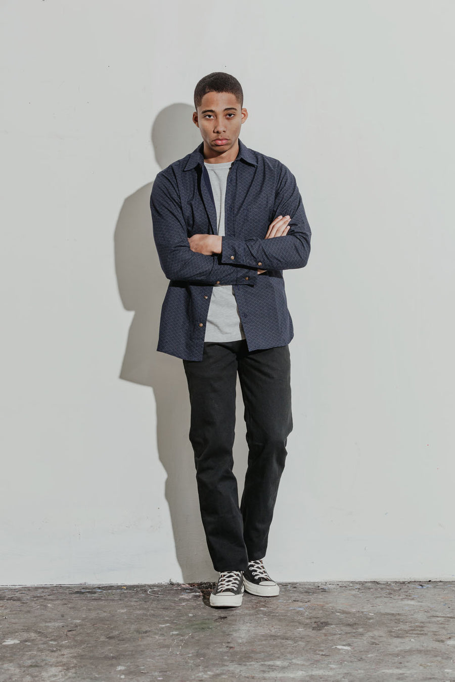 Model wears a heather grey tee under a printed button down long sleeve shirt, coupled with dark chinos.