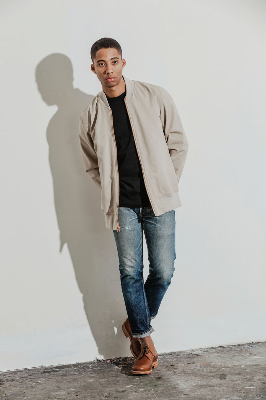 Model poses with a black tee, khaki bomber jacket and worn-in jeans.