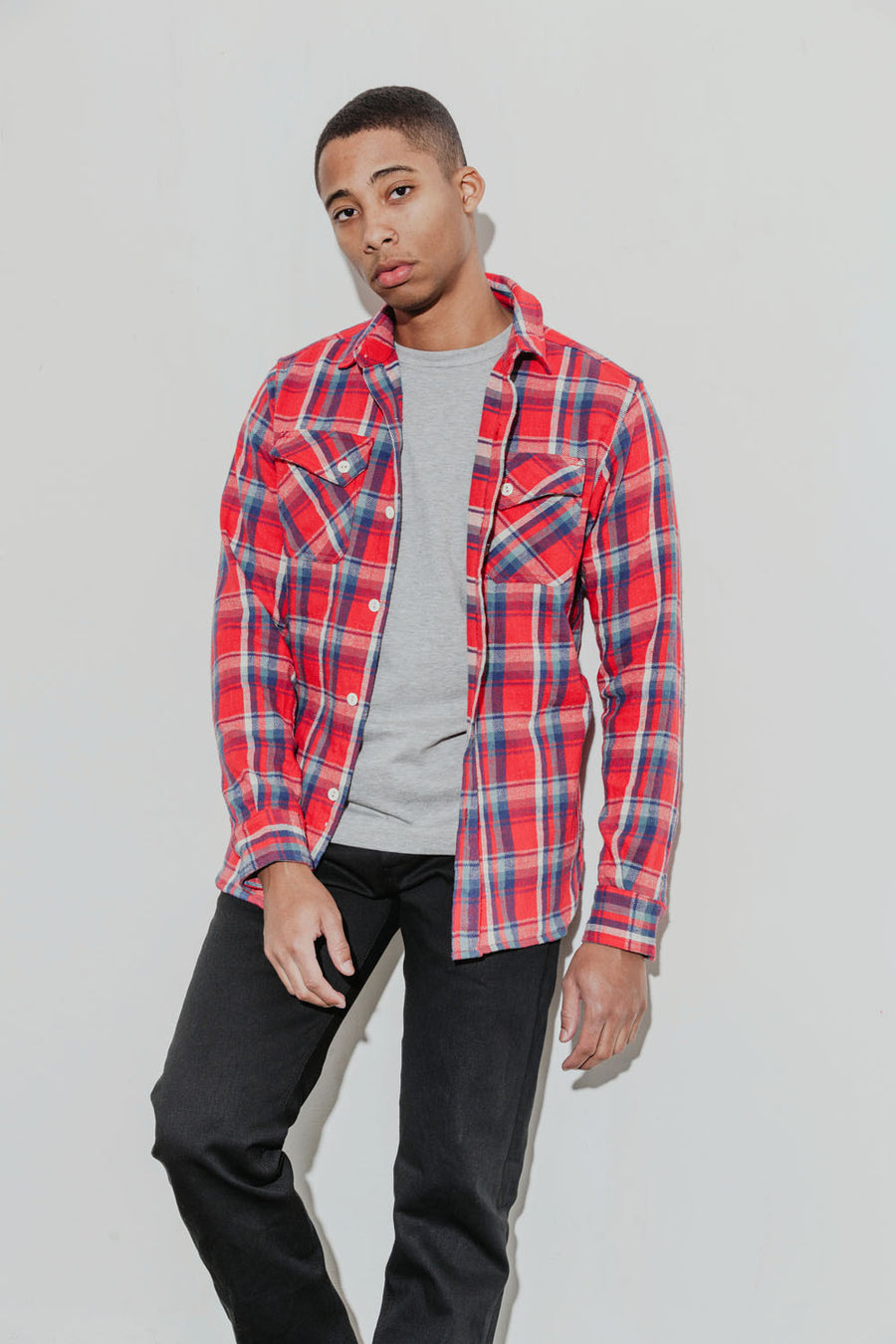 Model wears a grey tee under a bright red plaid flannel with black chinos.