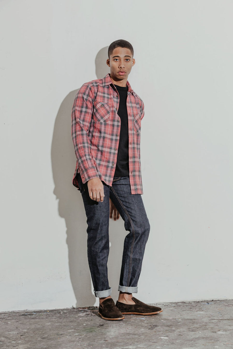 Model wears a faded red plaid shirt with a black tee and indigo jeans.