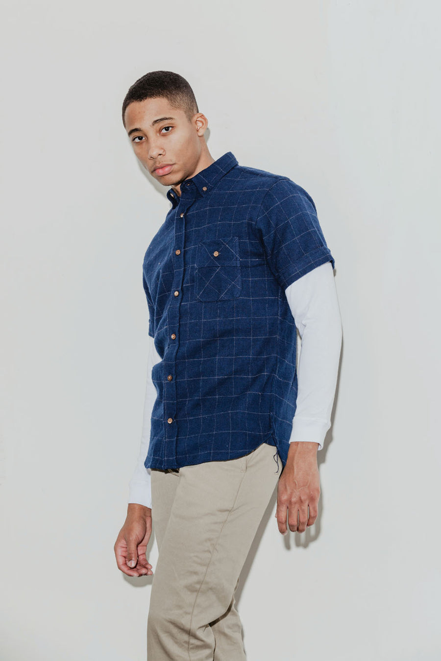 Model wears a long sleeve thermal layered under a navy short sleeve windowpane plaid shirt.