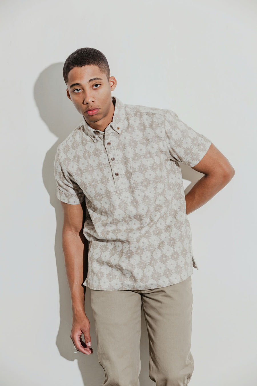 Model wears a tan aztec patterned popover shirt and tan khaki pants..