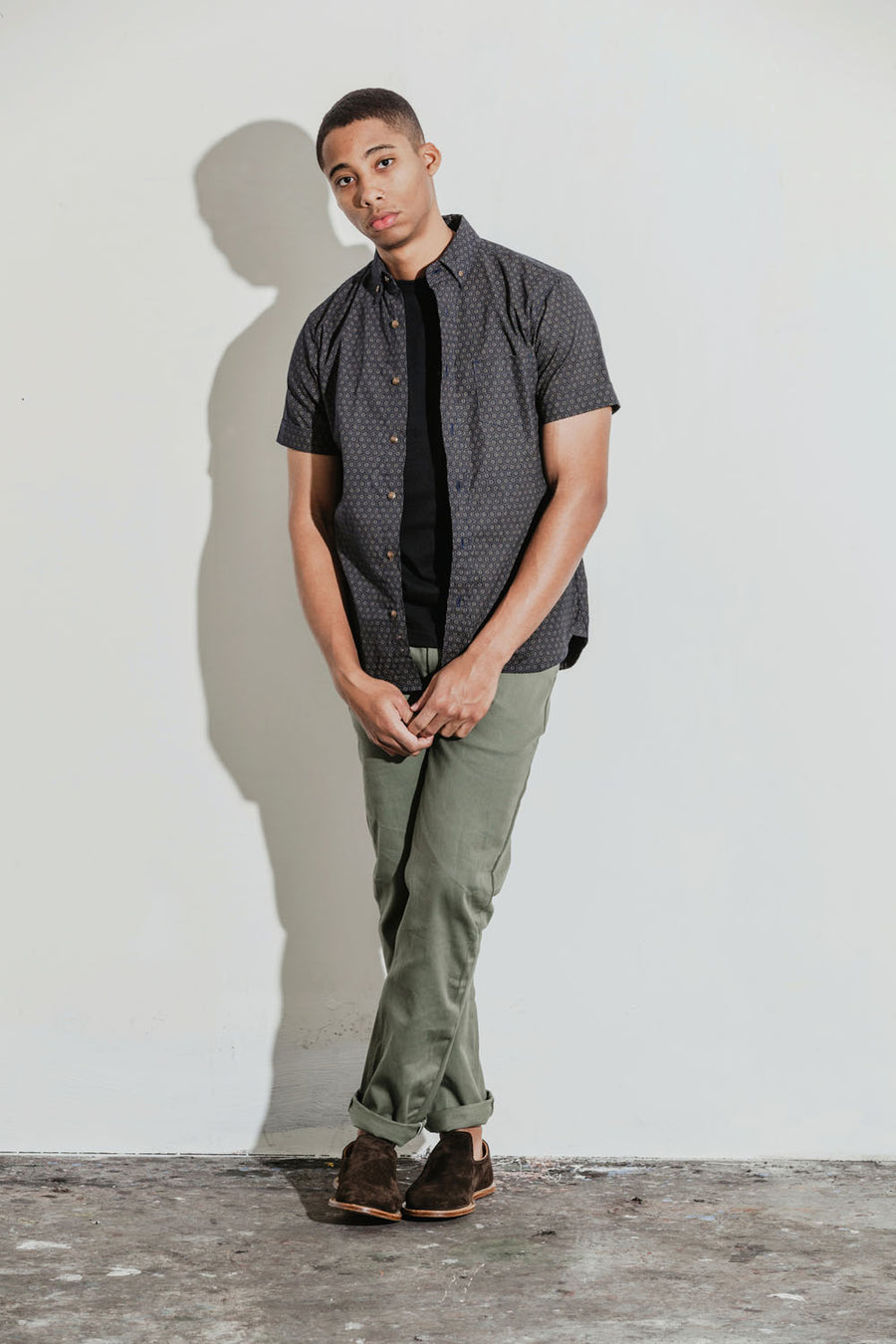 Model wears a patterned short sleeve shirt in navy with olive chinos.