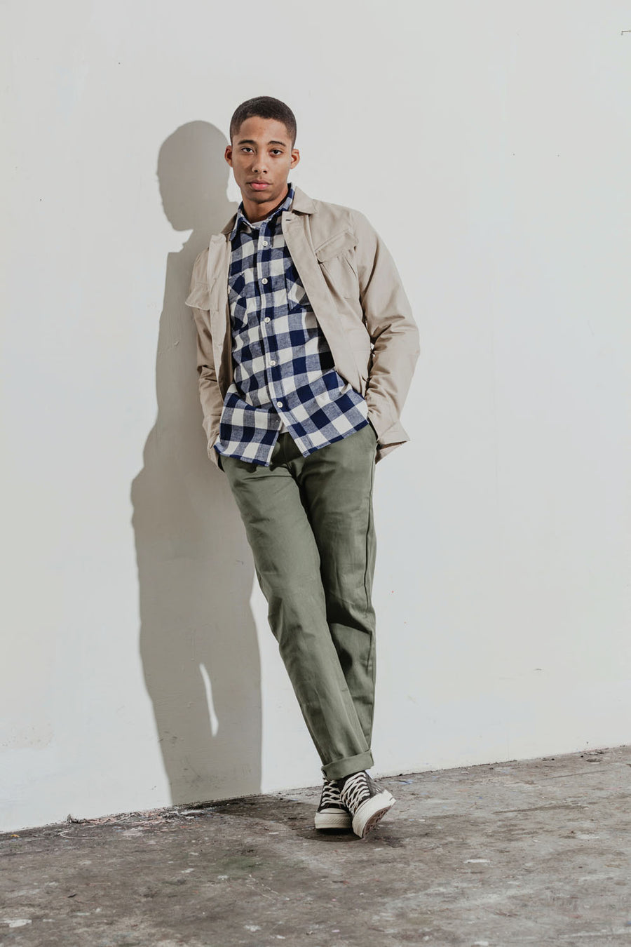 Model wears a navy plaid shirt under a khaki jacket.