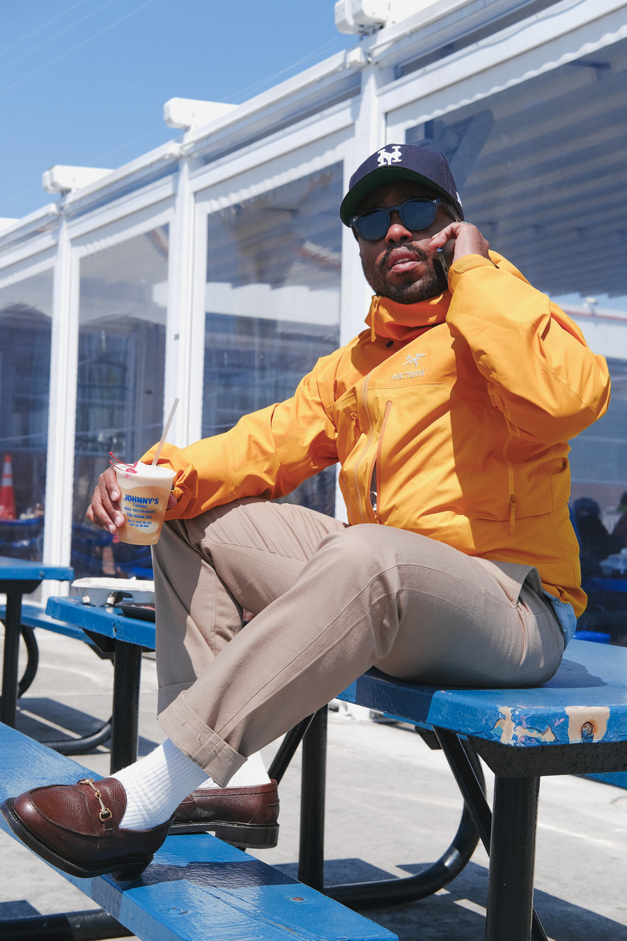 A man in a yellow jacket sits on a picnic table talking on the phone.