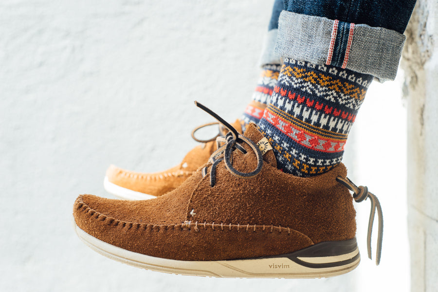 A closeup shot of navy patterned knit socks with tan suede sneakers.
