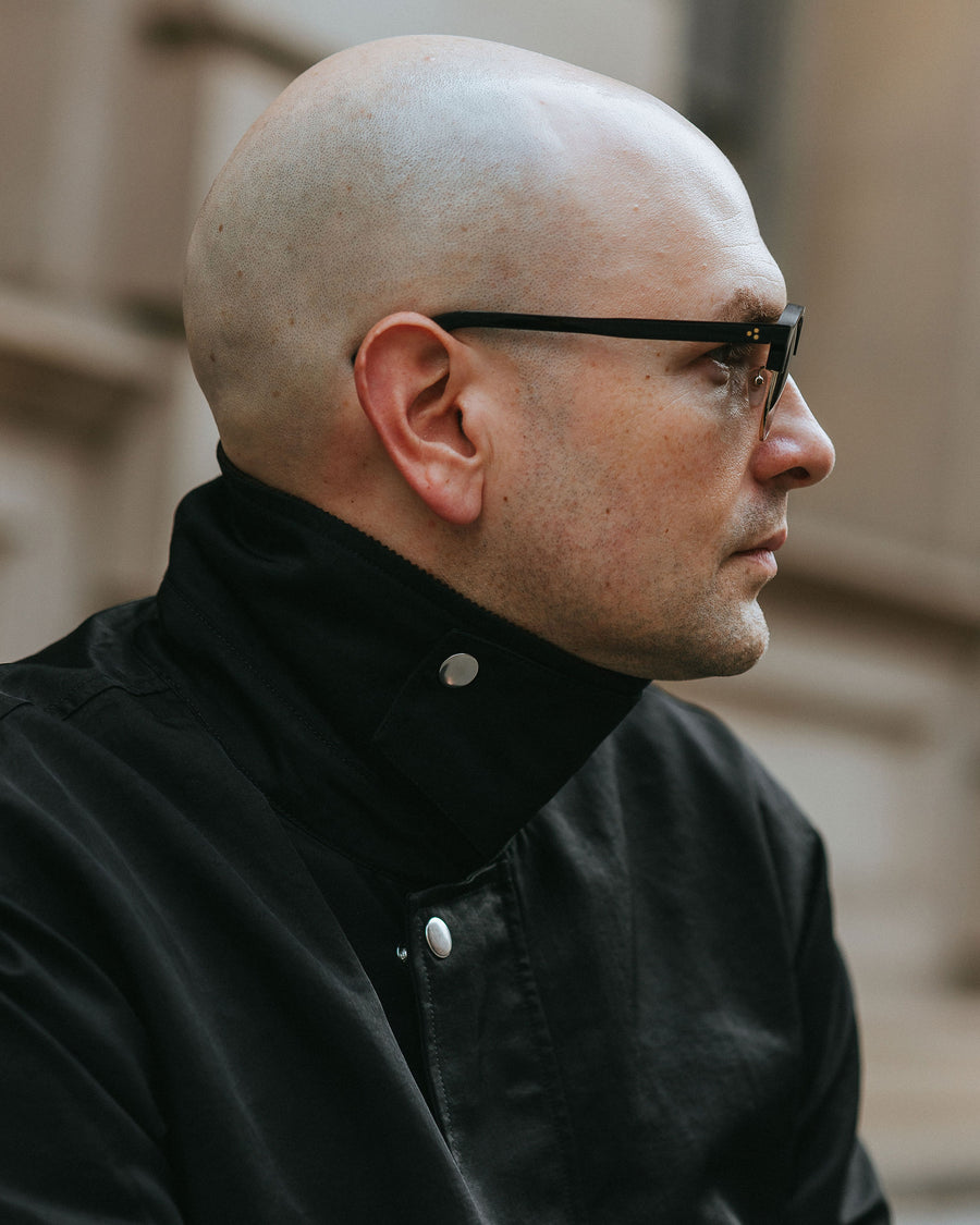 A side profile image of a man in black sunglasses.