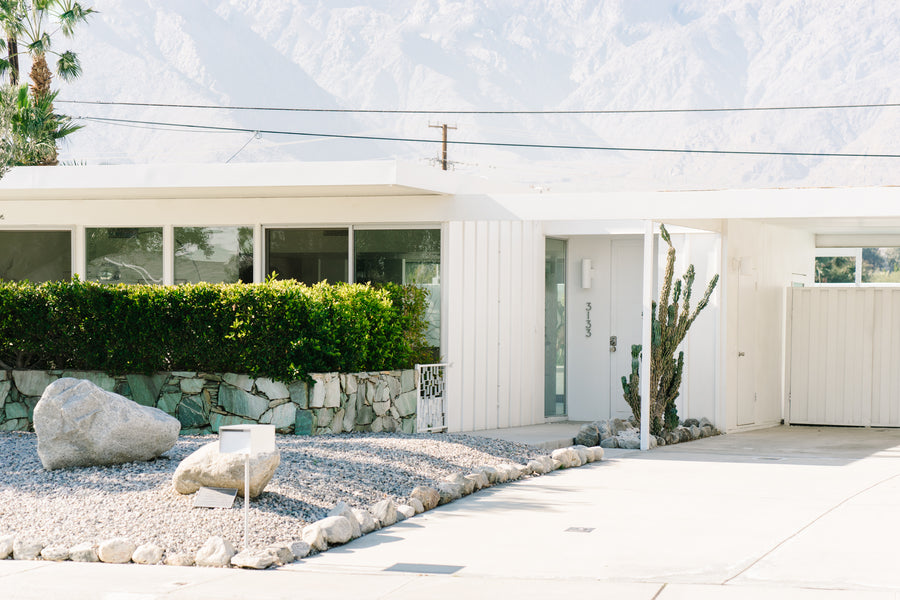 A white mid century home with a front yard full of rocks.