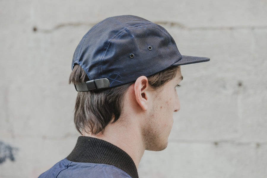 Profile shot of model wearing the navy waxed canvas 5-panel with embroidered pickaxe detail.