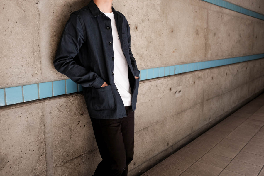 Model is leaning against a wall while wearing the navy work jacket.