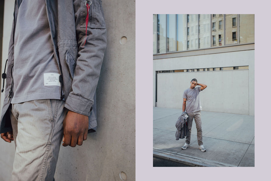 A man stands in front of a concrete building in grey tee and chinos
