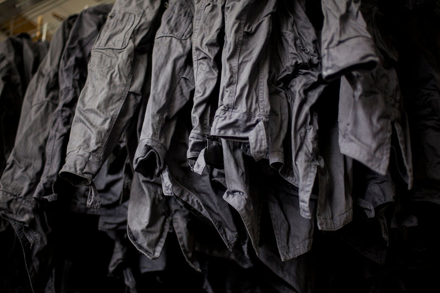 A sea of freshly dyed grey jackets hang from the ceiling.