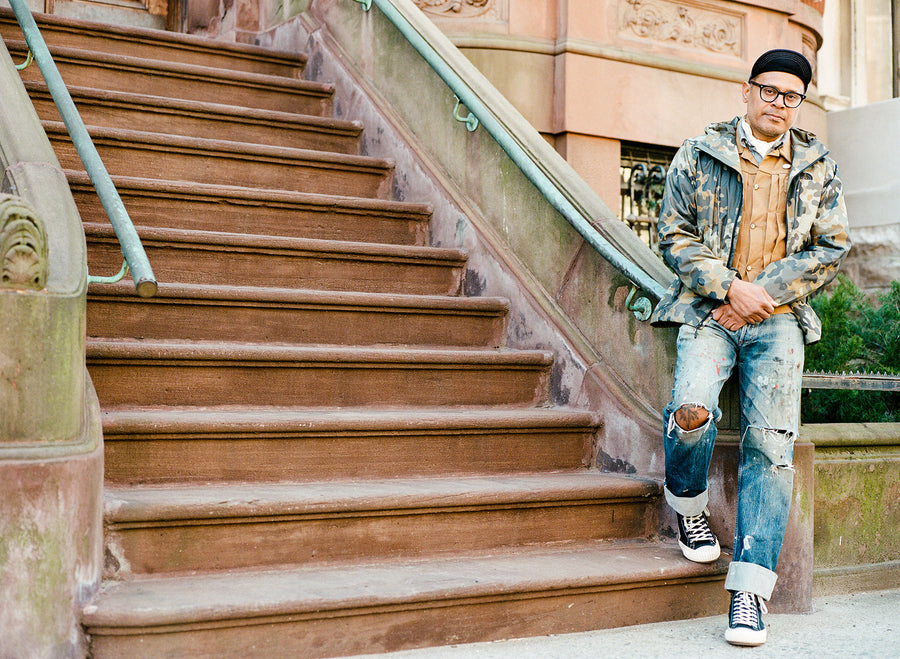 A man stands at the foot of some brownstone stairs. 