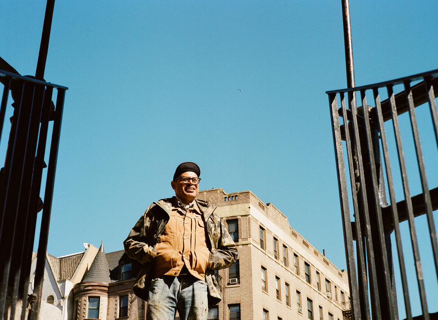 A man in a camo jacket stands against a bright blue sky, smiling.