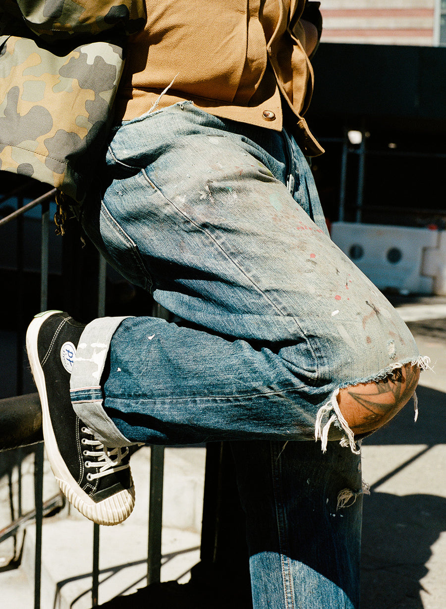 A worn in pair of jeans with the knees ripped to reveal a tattooed knee behind.