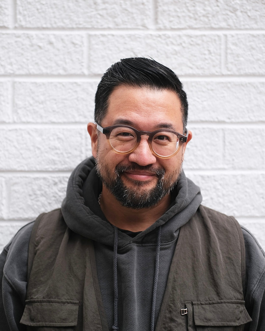 An asian man in front of a white wall.