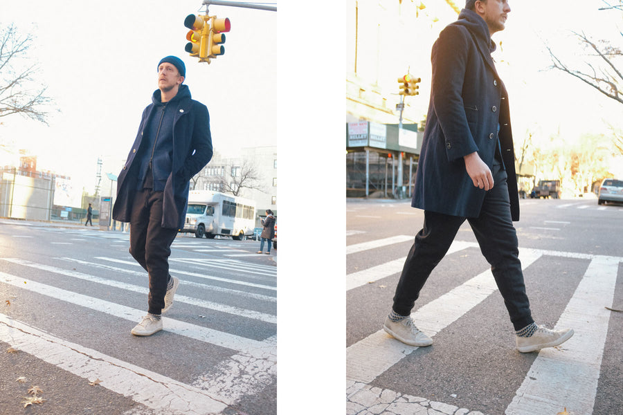 The model crosses the street wearing the black sweatpants as the sun sets.